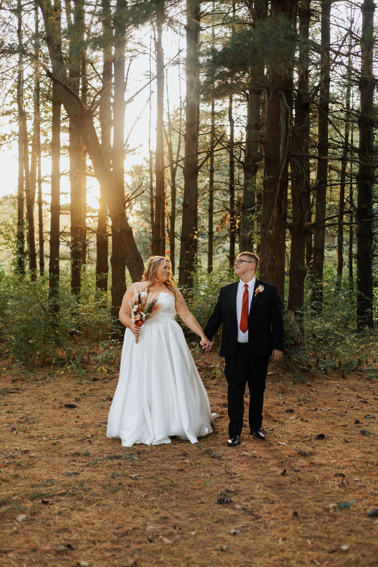 Couple takes romantic wedding photos in a sunlit forest with pine trees creating a magical backdrop.
