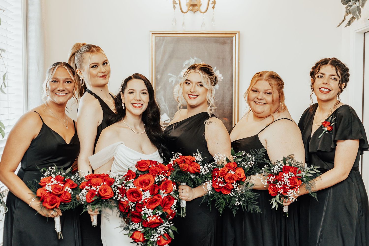 Wedding party in black dresses holding vibrant red bouquets.