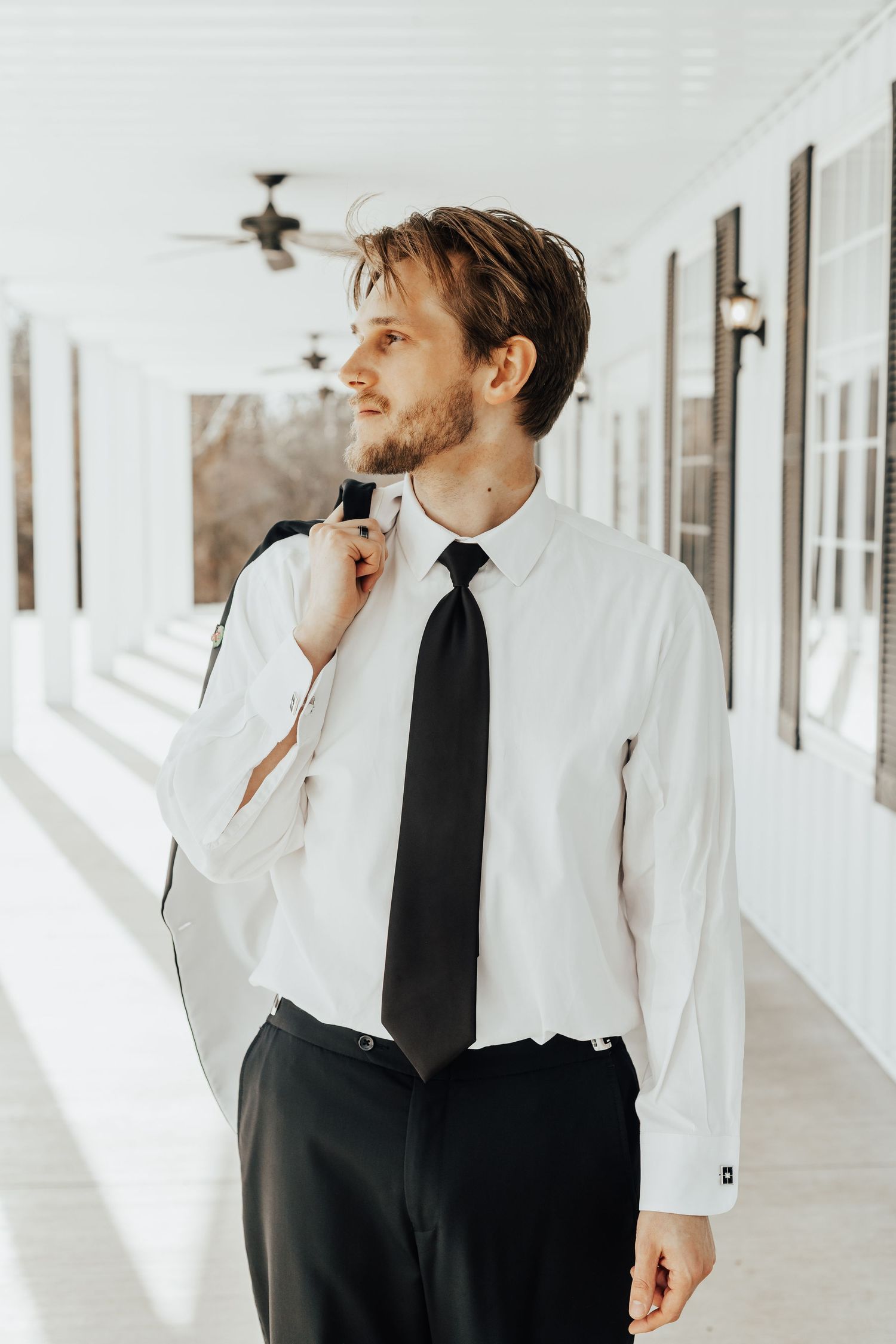 Artistic groom portraits in a white corridor showing contemplative poses in classic black and white attire.