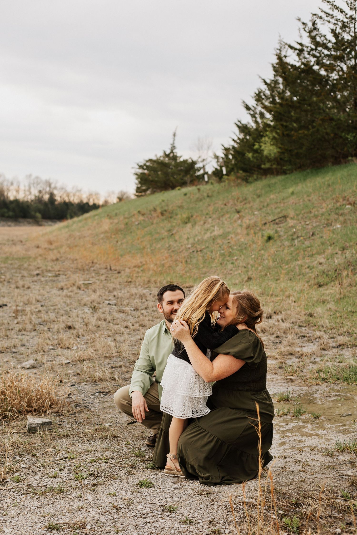 Family photo session on hillside with overcast sky background.