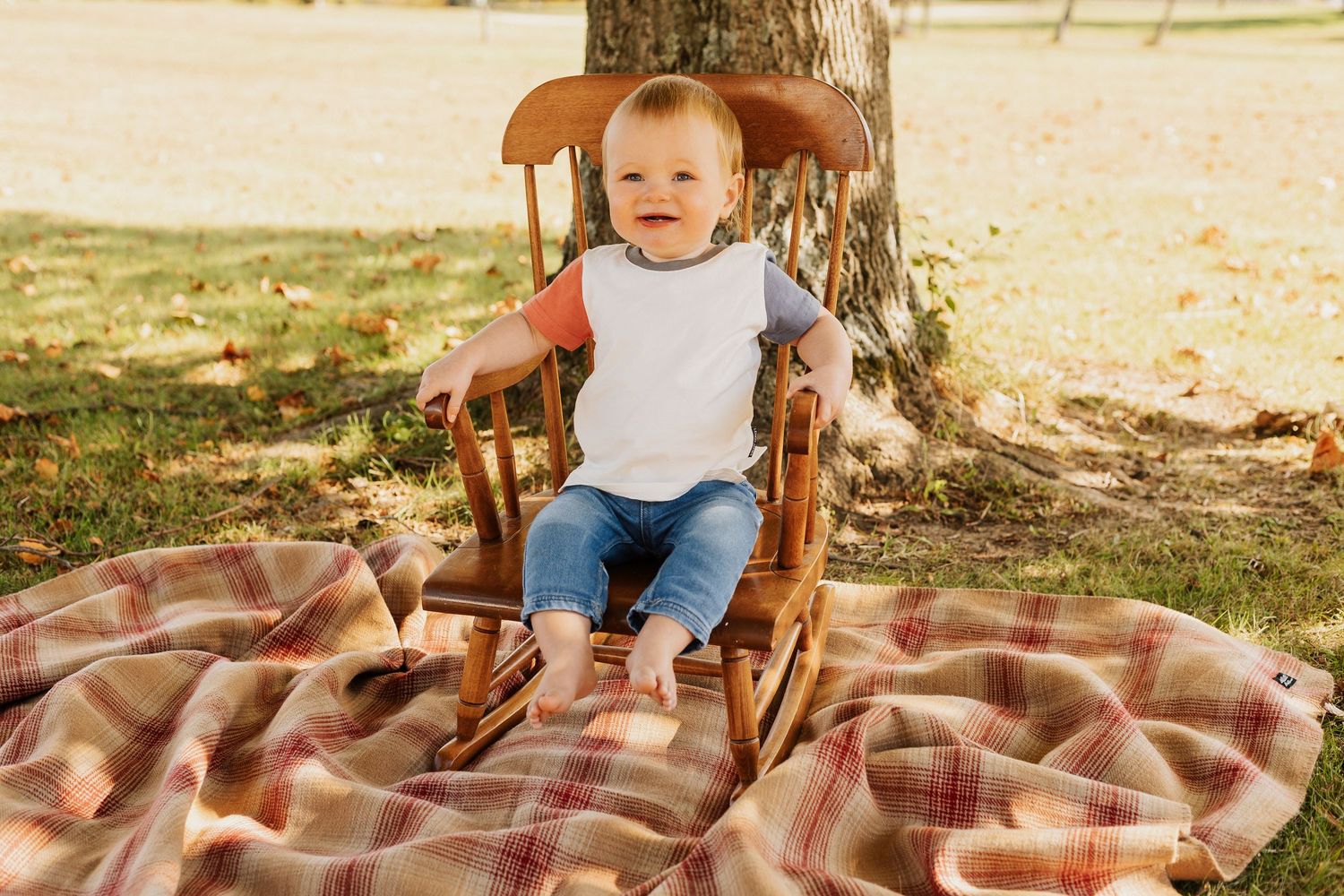 Baby sitting on plaid blanket during outdoor autumn photoshoot.