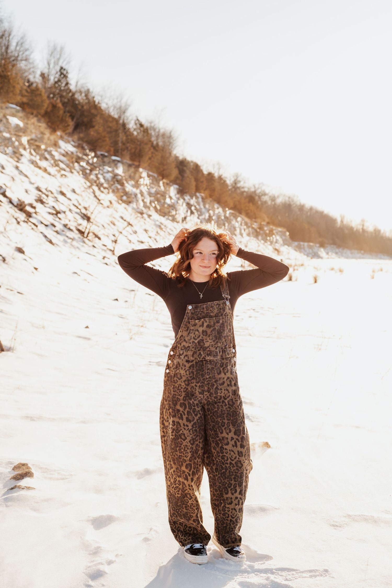 Winter portrait session with someone posing playfully in the snow wearing a patterned jumpsuit.
