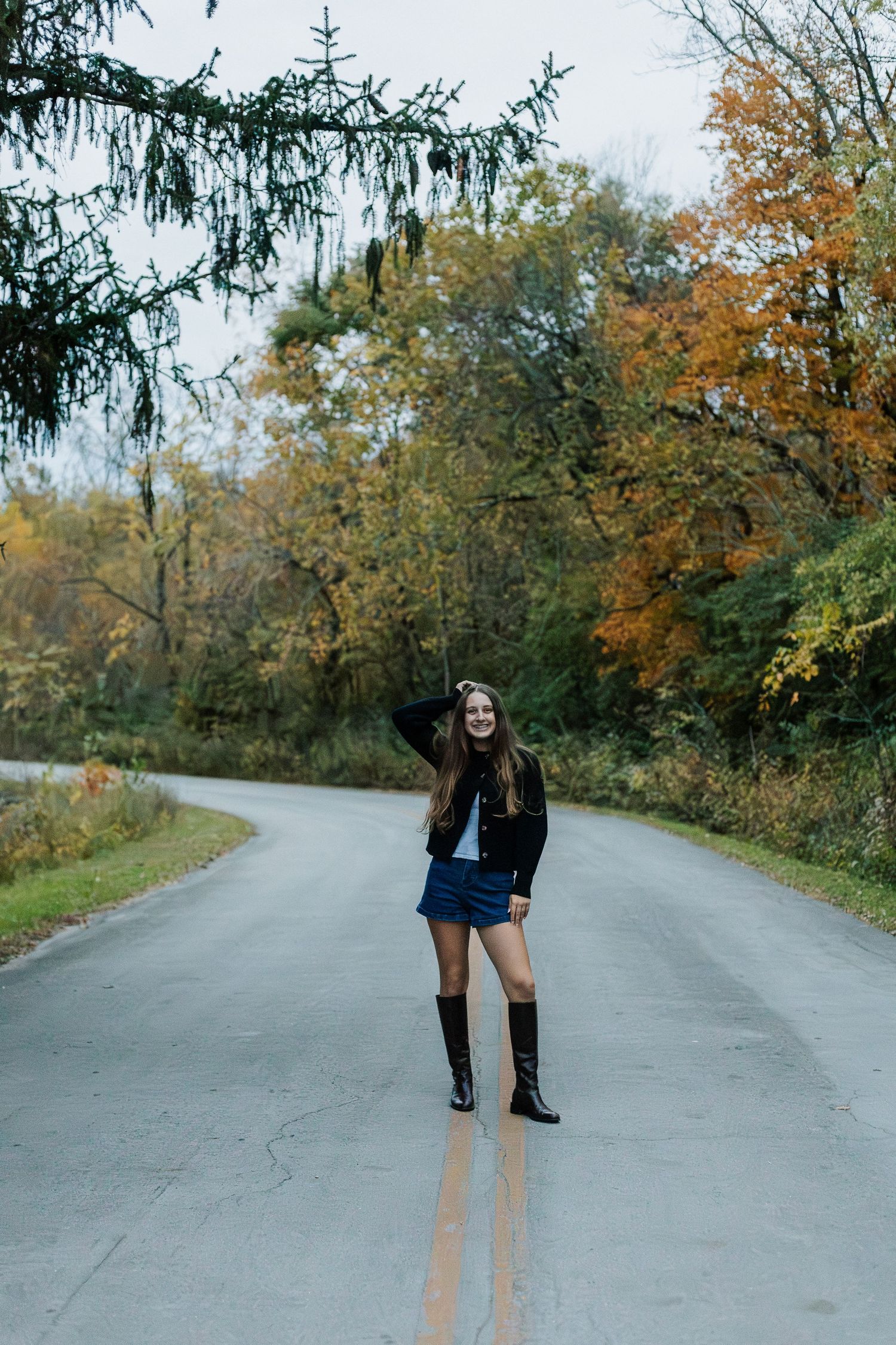 Person posing on empty road surrounded by autumn trees and fall colors.