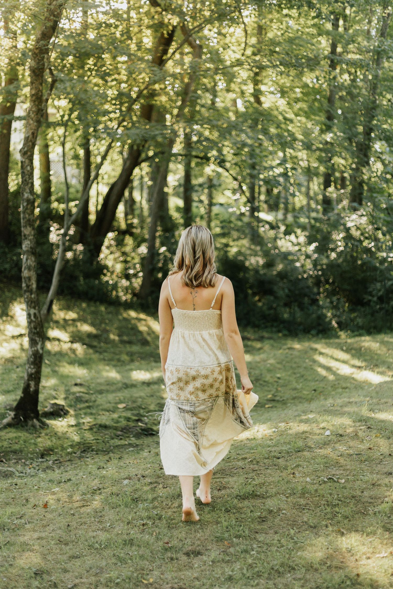 Woman in flowing white dress walks through wooded path carrying basket.