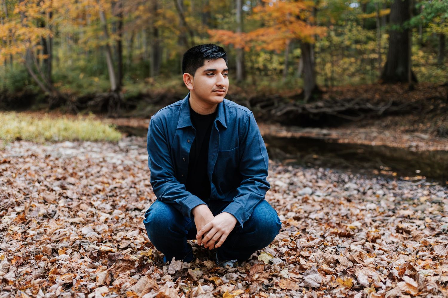 Person sitting cross-legged on autumn leaves wearing denim and navy jacket.