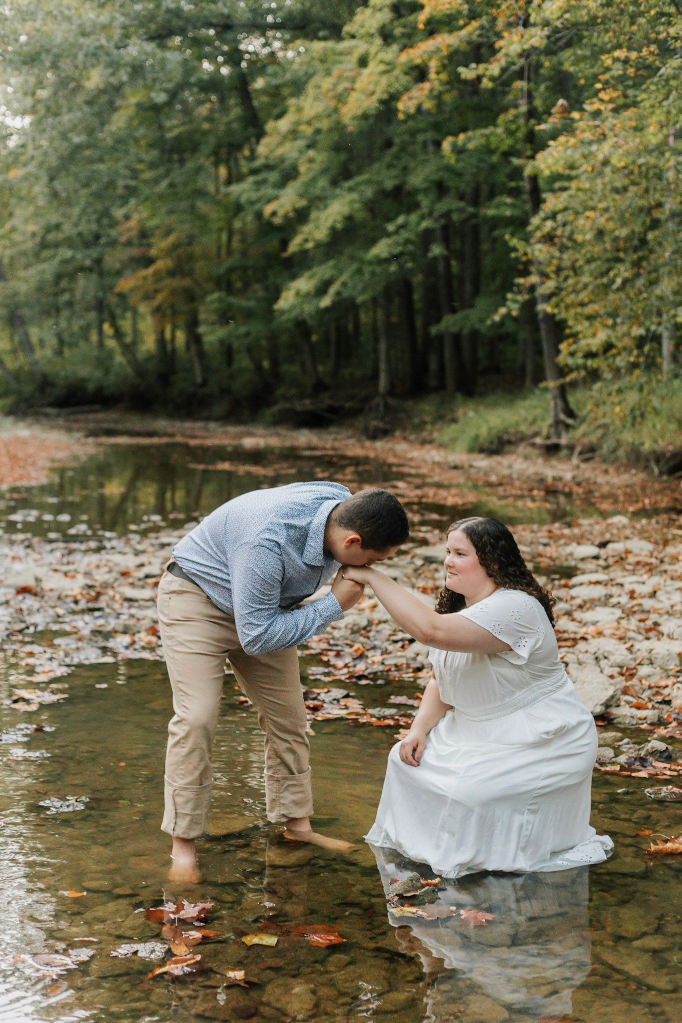 A couple shares a playful moment in a creek surrounded by fall foliage.