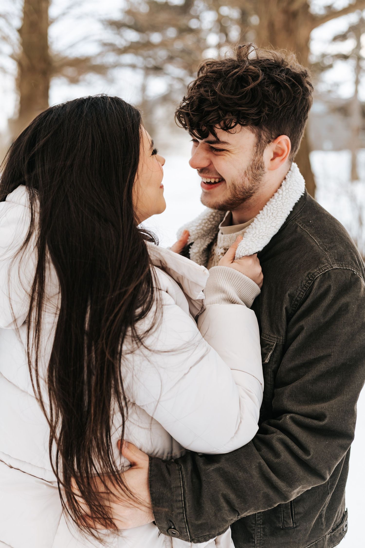 A romantic winter couple moment sharing laughter in a snowy forest setting.