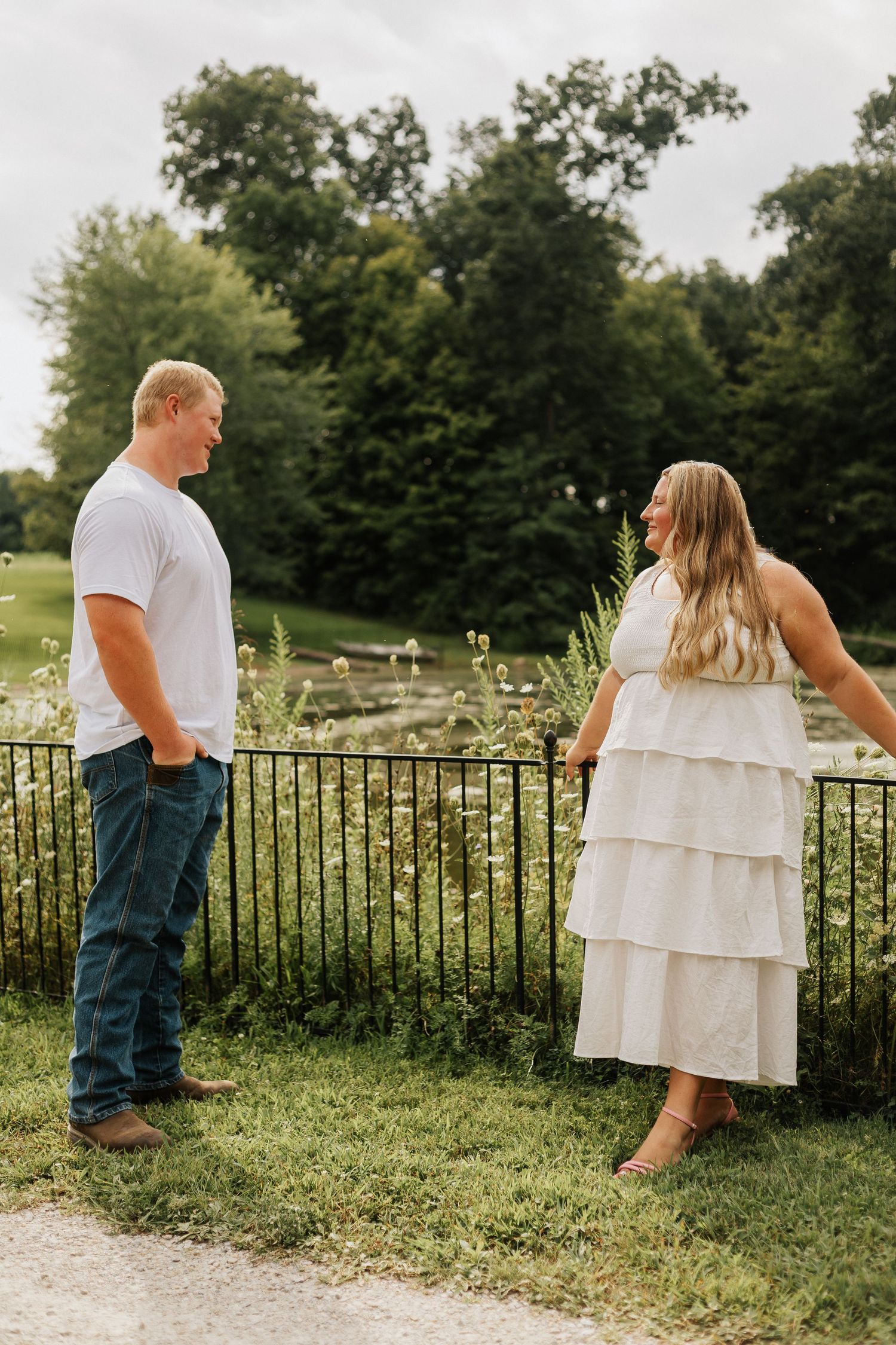 A couple walks along a fence-lined path in a park setting.