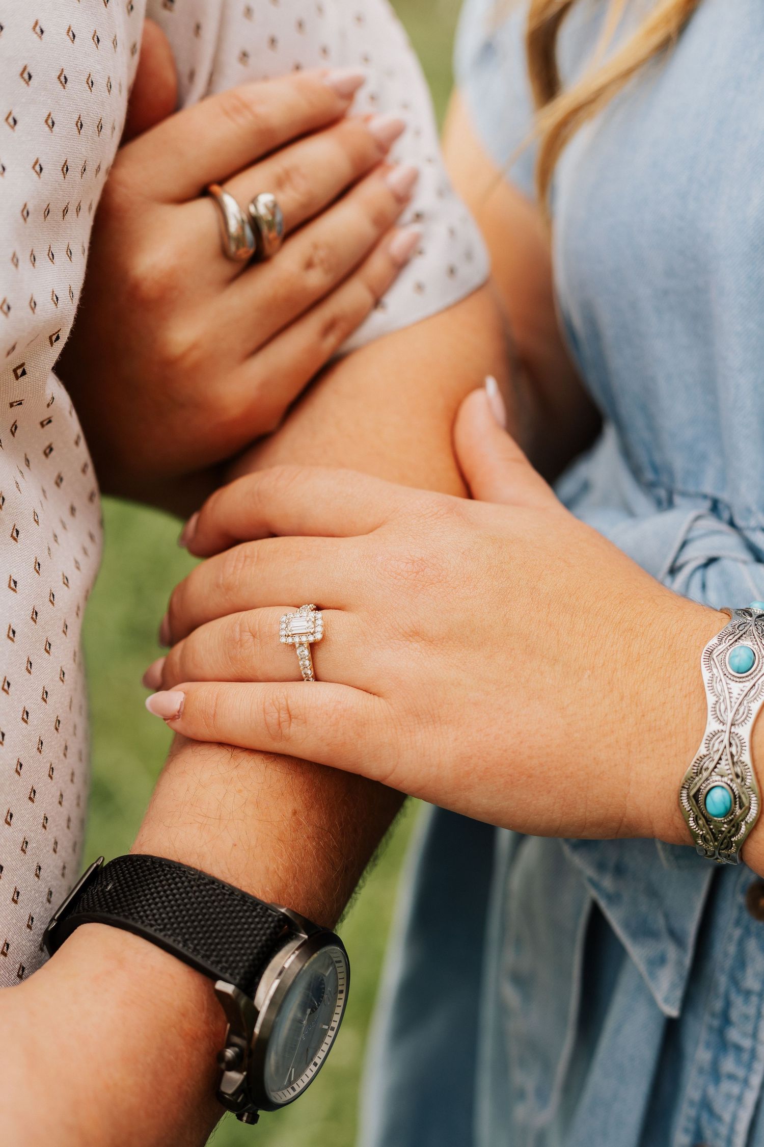 Close-up of hands showing engagement rings and turquoise bracelet jewelry against casual clothing.