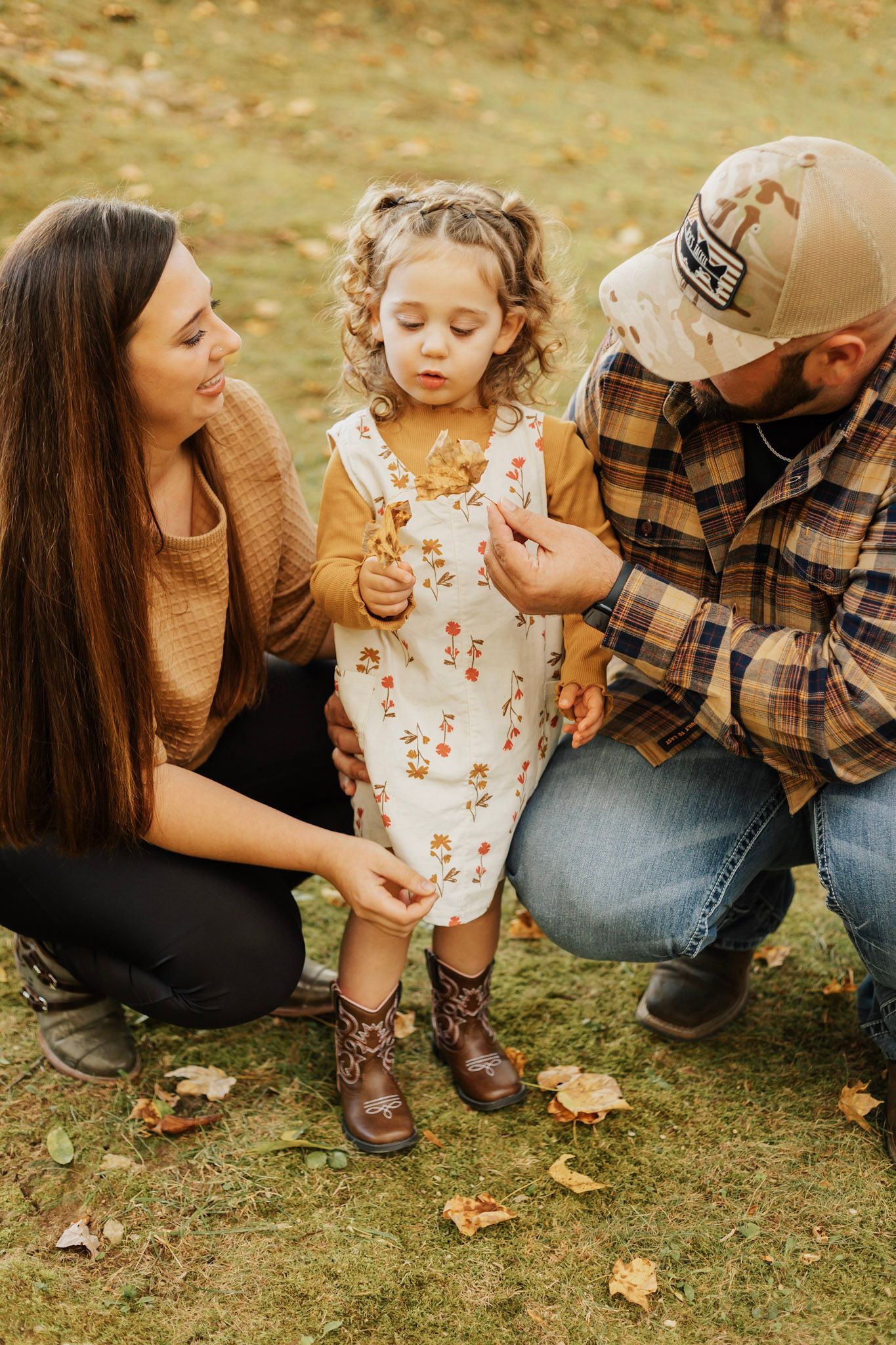 Casual family photo session on grass with autumn leaves and coordinated fall outfits.