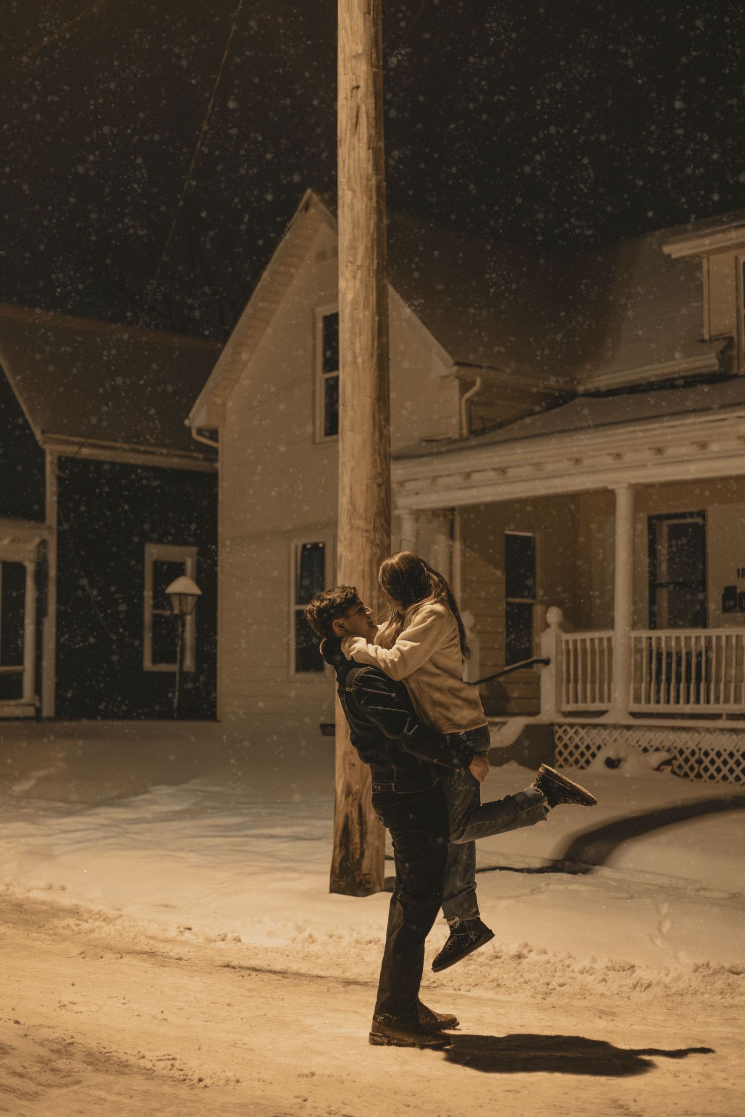 Sequence of silhouettes showing a person jumping in the snow at night in front of suburban houses.