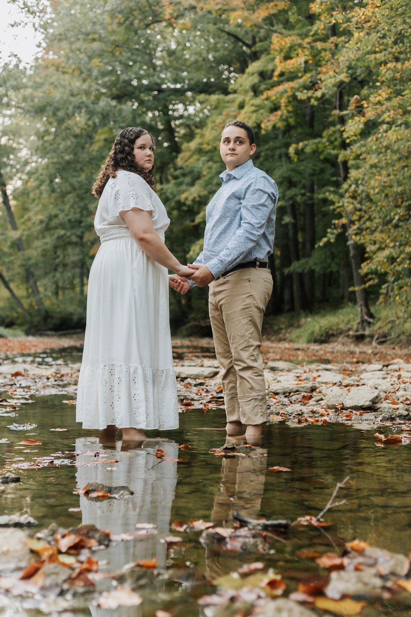 Couple standing in shallow creek water surrounded by autumn leaves.