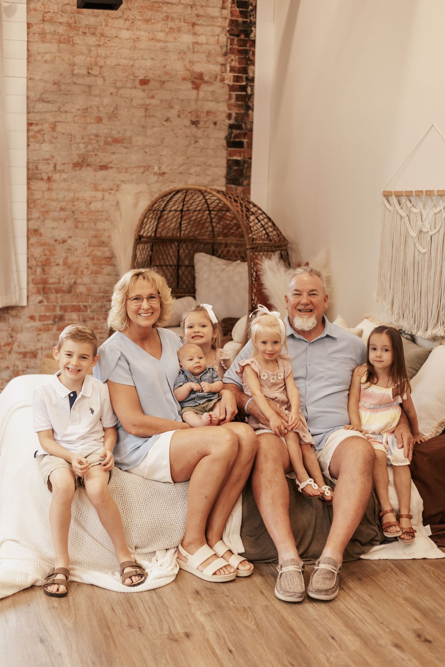 Extended family gathered on a couch for a casual indoor portrait against exposed brick walls.