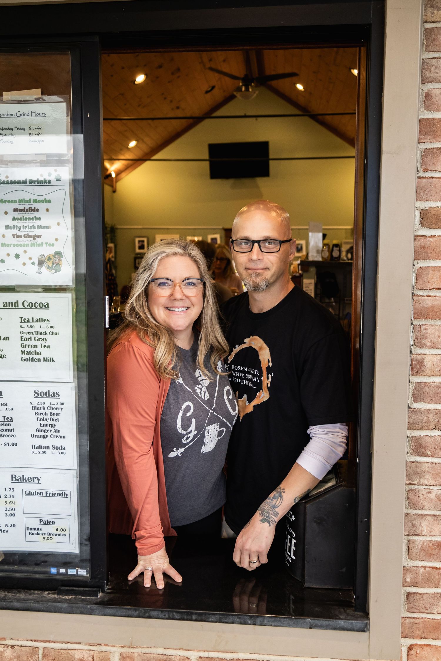 Coffee shop staff serving customers through service window with menu visible.