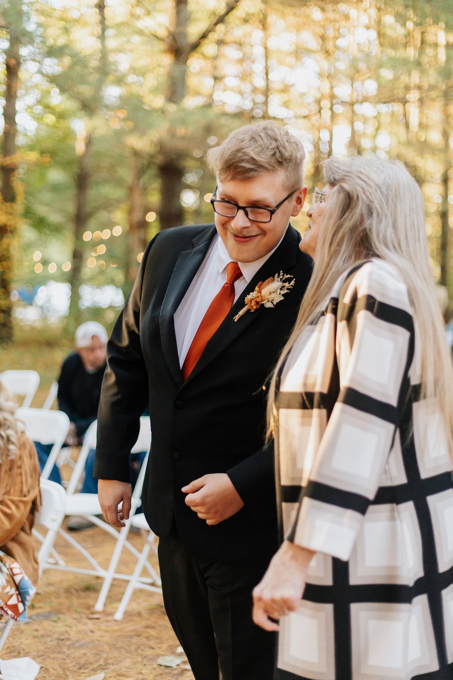 A couple shares a joyful moment at an outdoor autumn wedding ceremony with folding chairs.