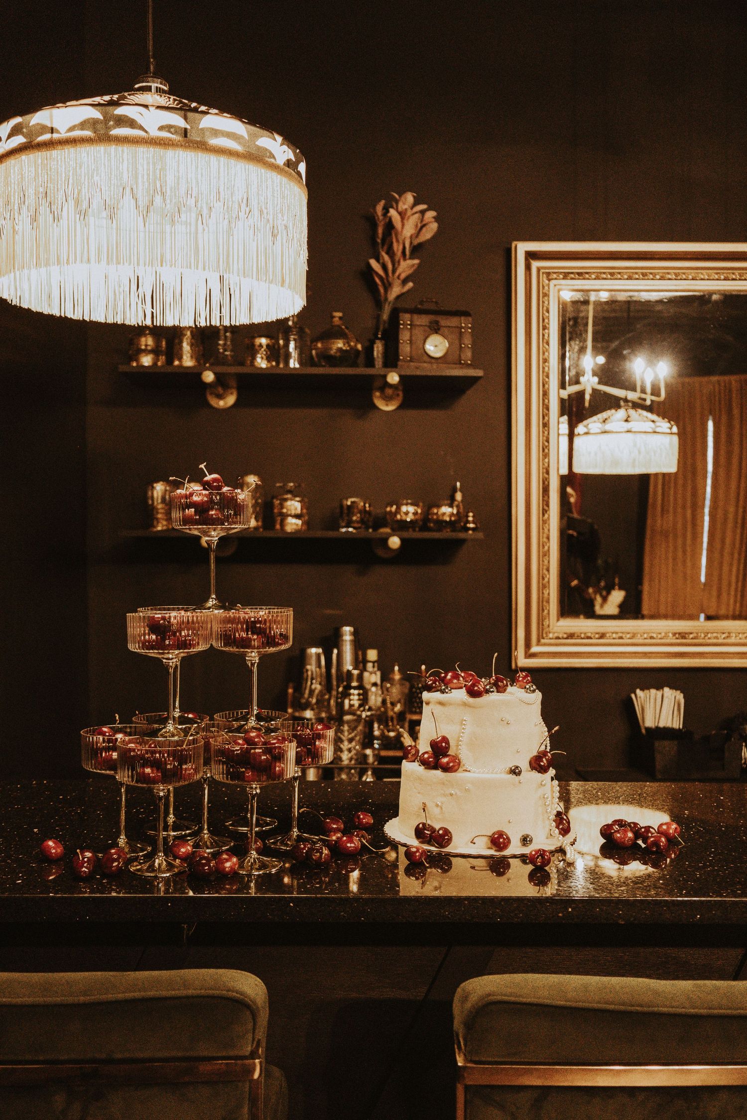 Wedding cake and tiered crystal stands with cherries under vintage chandelier lighting.