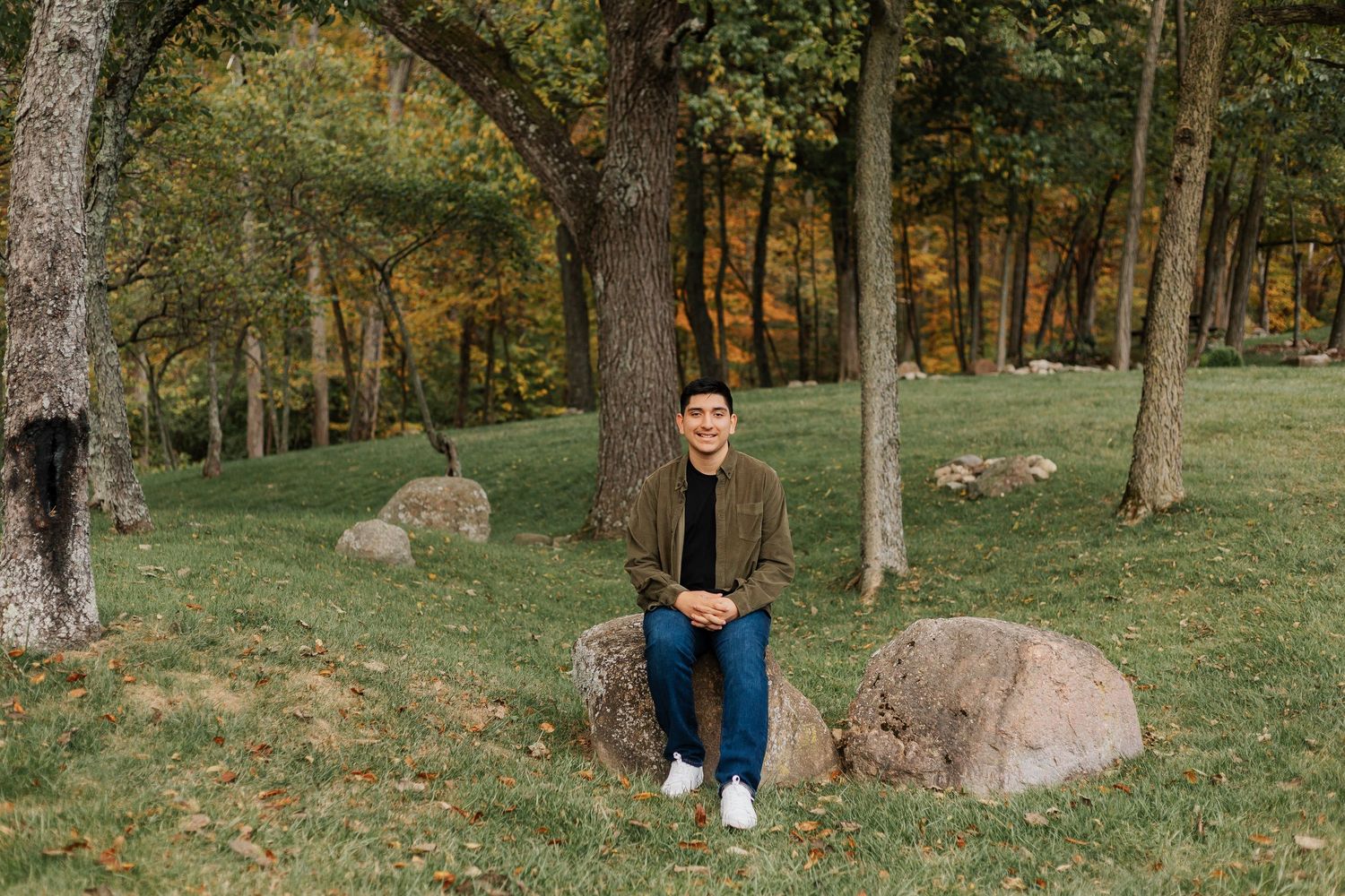 Person sitting on rock in wooded park during autumn season.