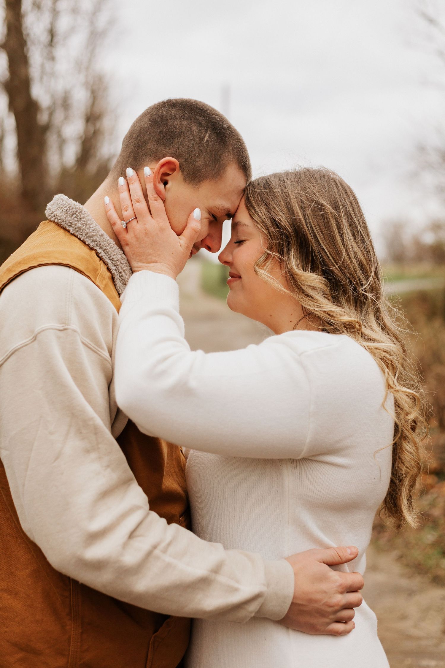 Intimate embrace captured in natural outdoor setting with autumn colors in background.