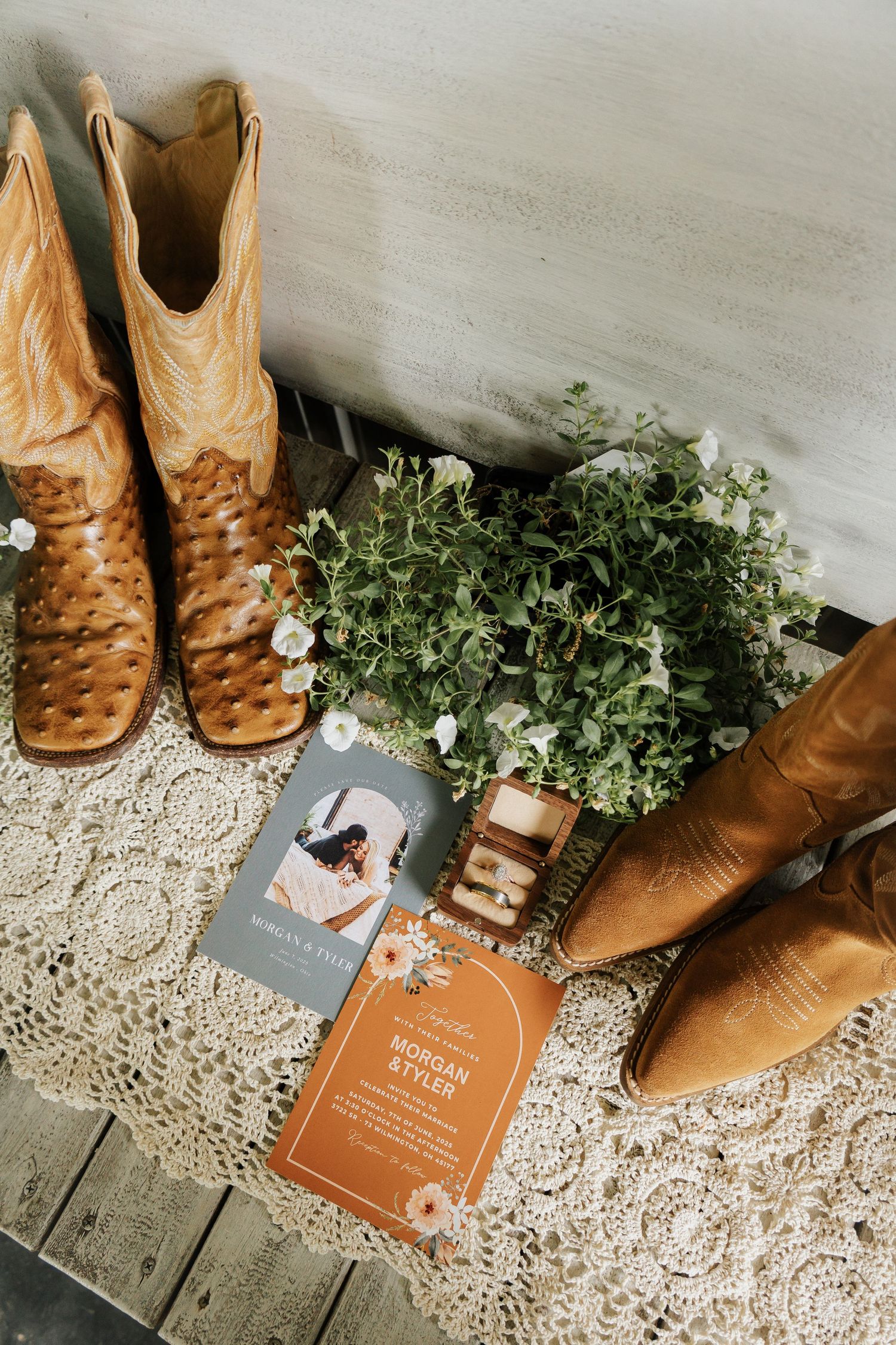 Wedding details featuring brown leather cowboy boots and invitation cards on lace backdrop.
