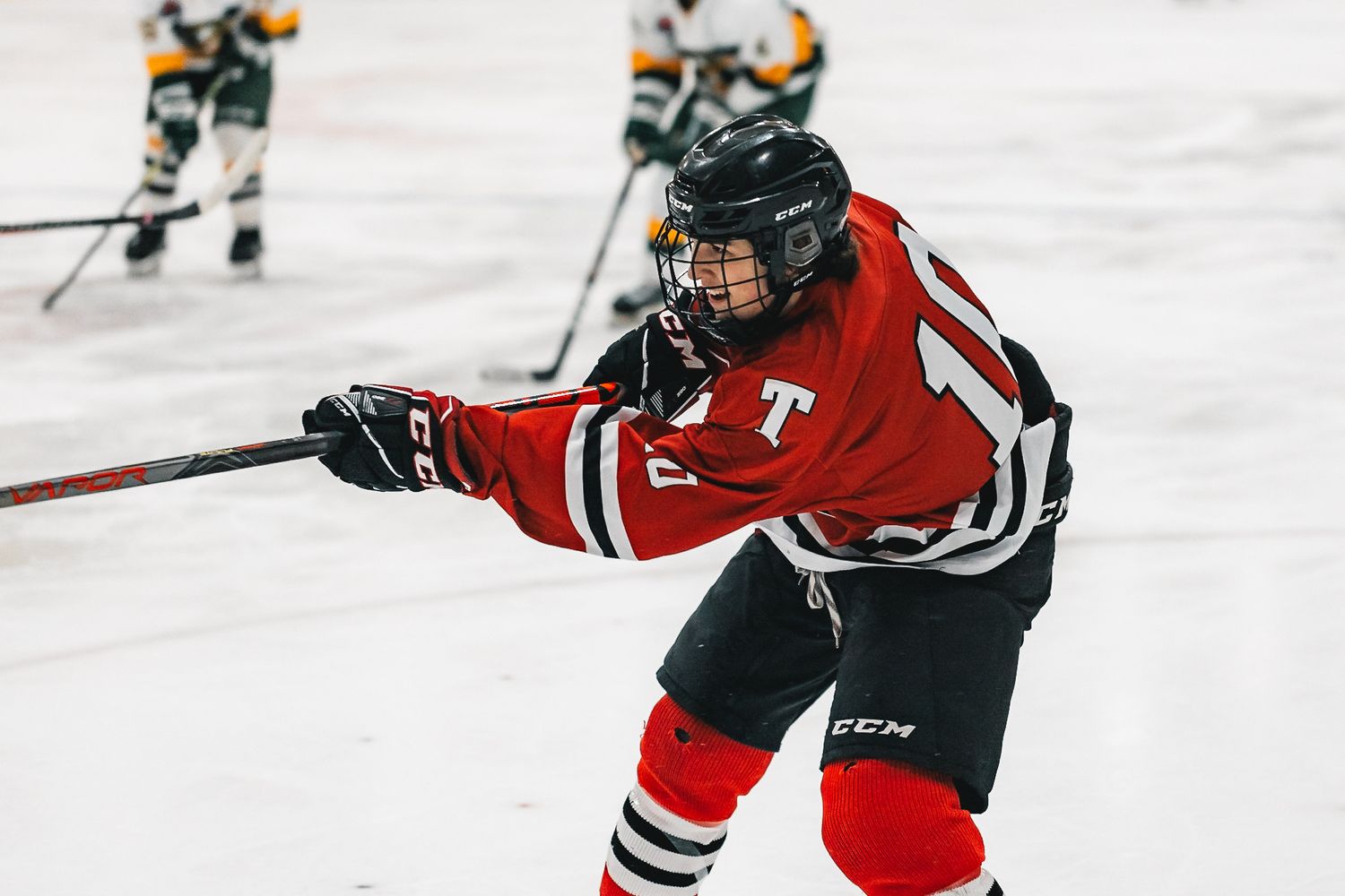 Hockey player in red jersey extends stick during intense game action.