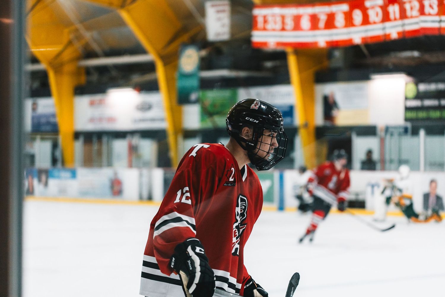 Hockey player in red and black jersey skating on ice rink during indoor game.