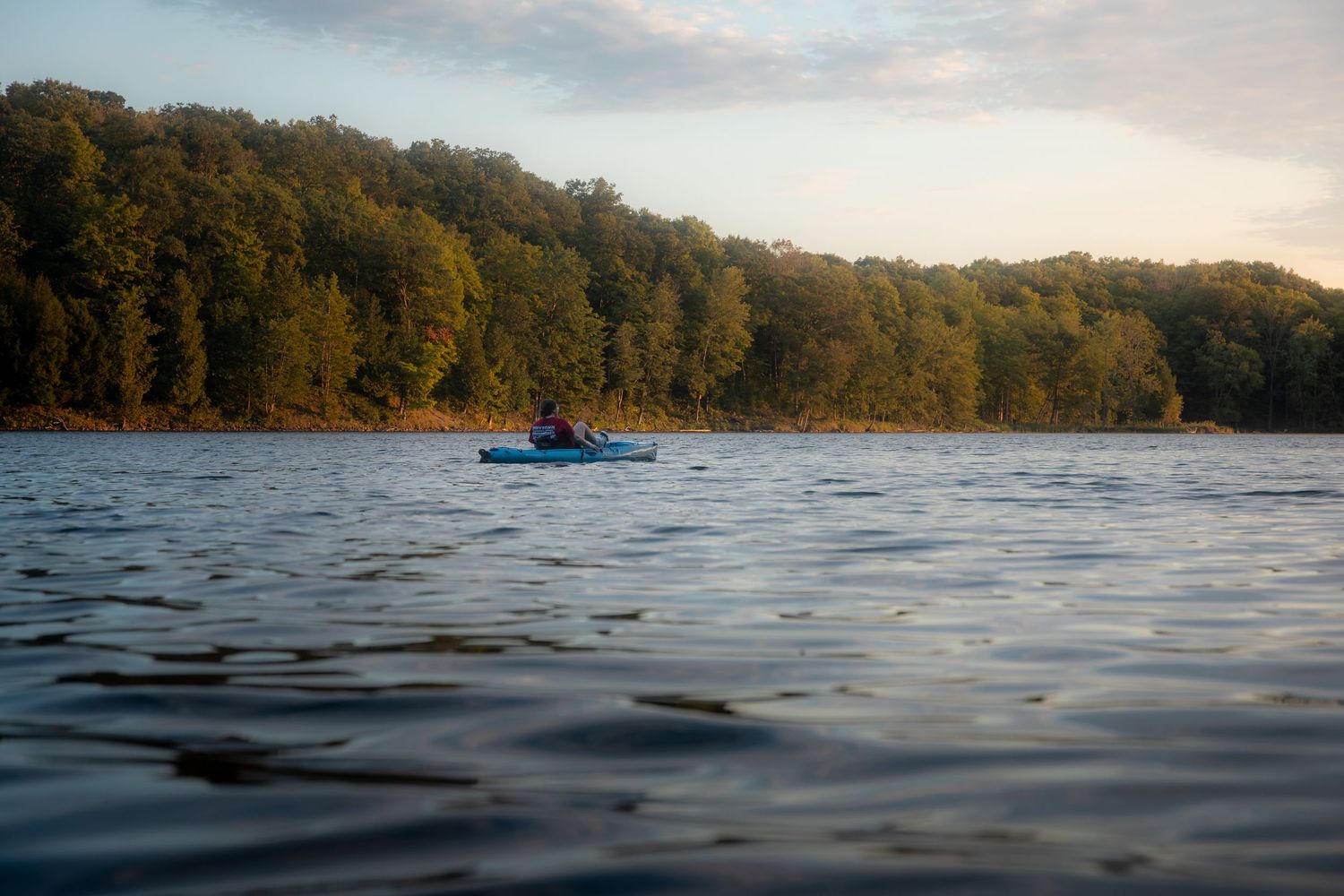 Tranquil lake scene with evergreen trees along the shore and rippling water in the foreground.