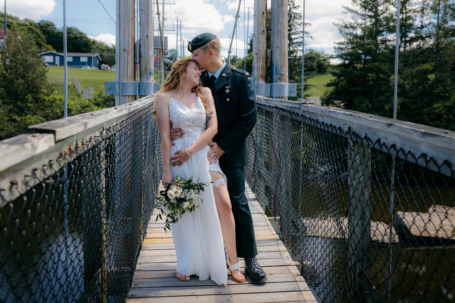 Wedding couple shares romantic moment on suspension bridge surrounded by trees.