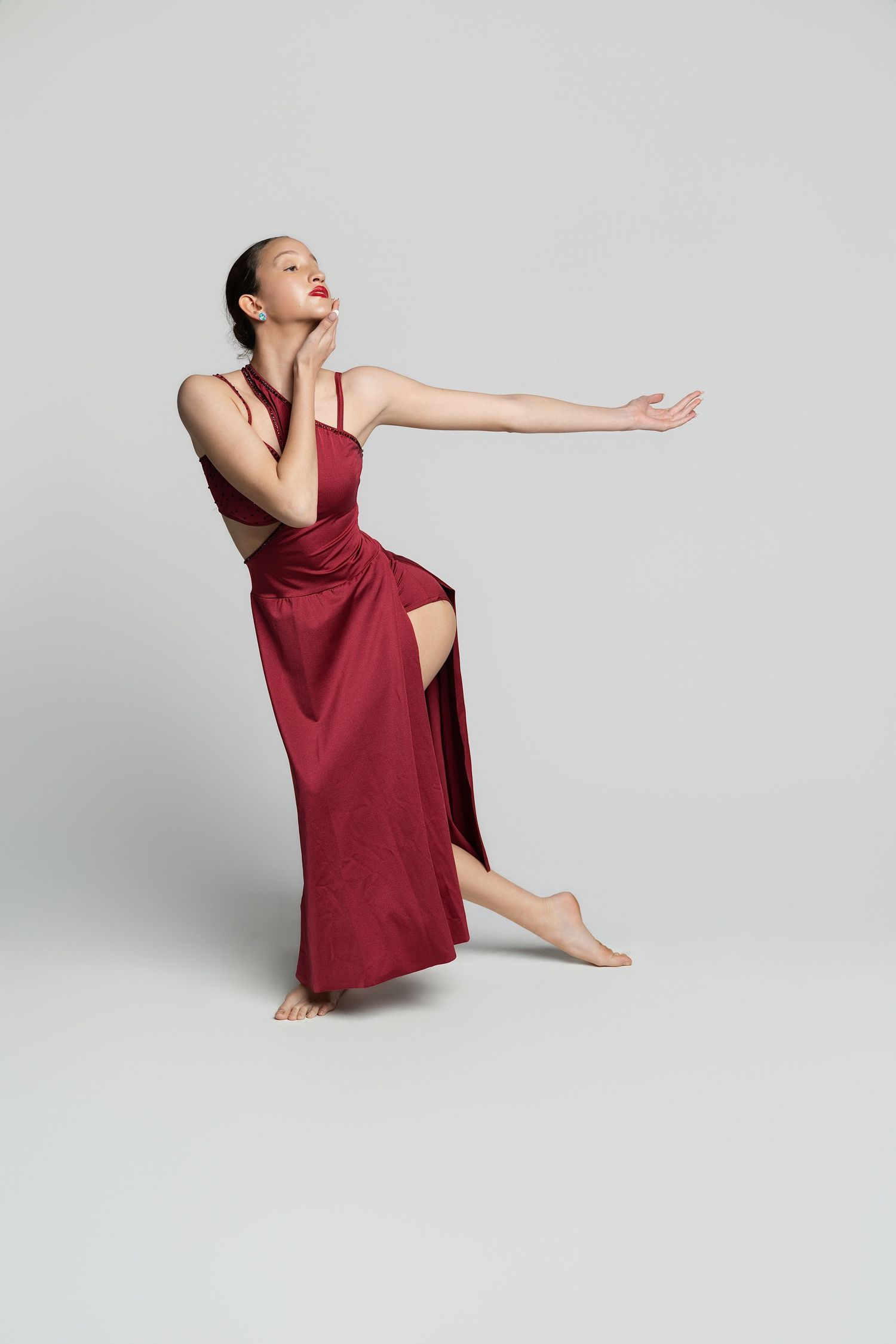 Dancer in a flowing red satin gown poses gracefully with arms extended on a light gray background.