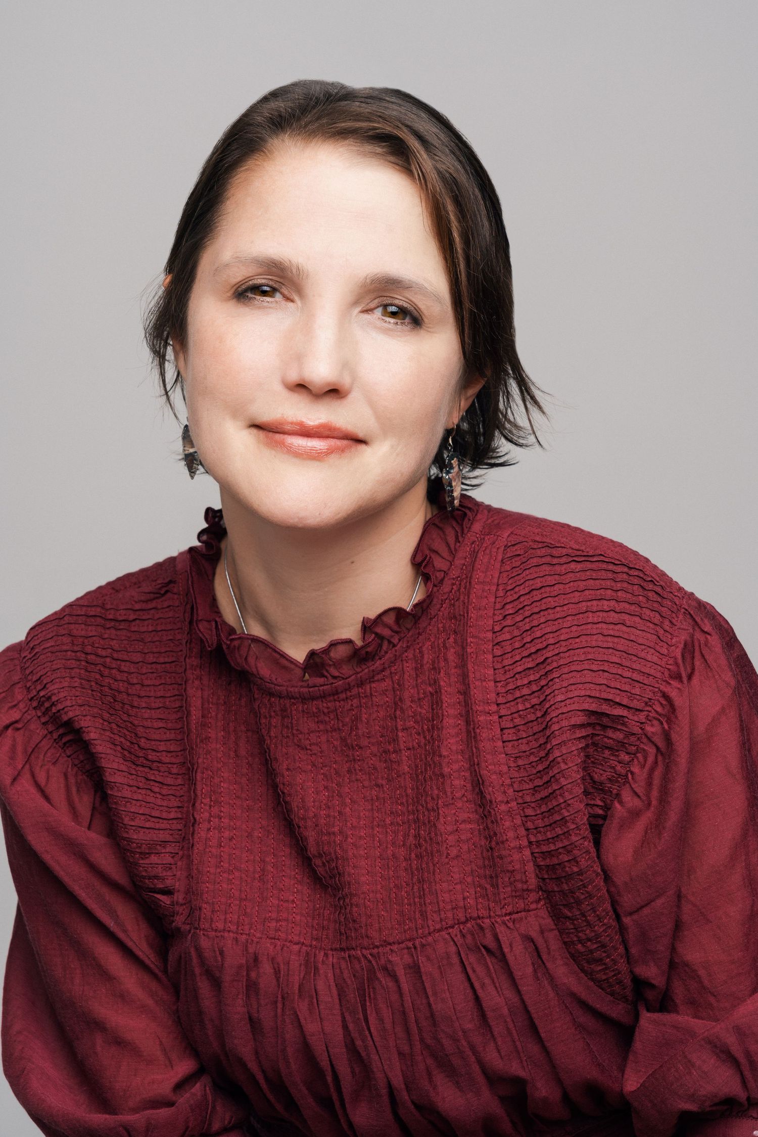 Portrait against grey background featuring person in burgundy ruffled blouse.