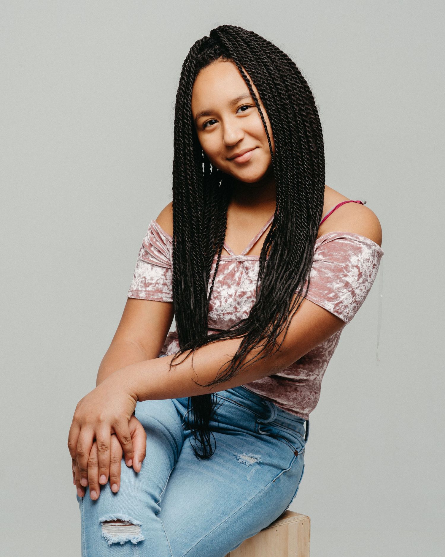 Portrait against gray background showing casual style and braided hair.