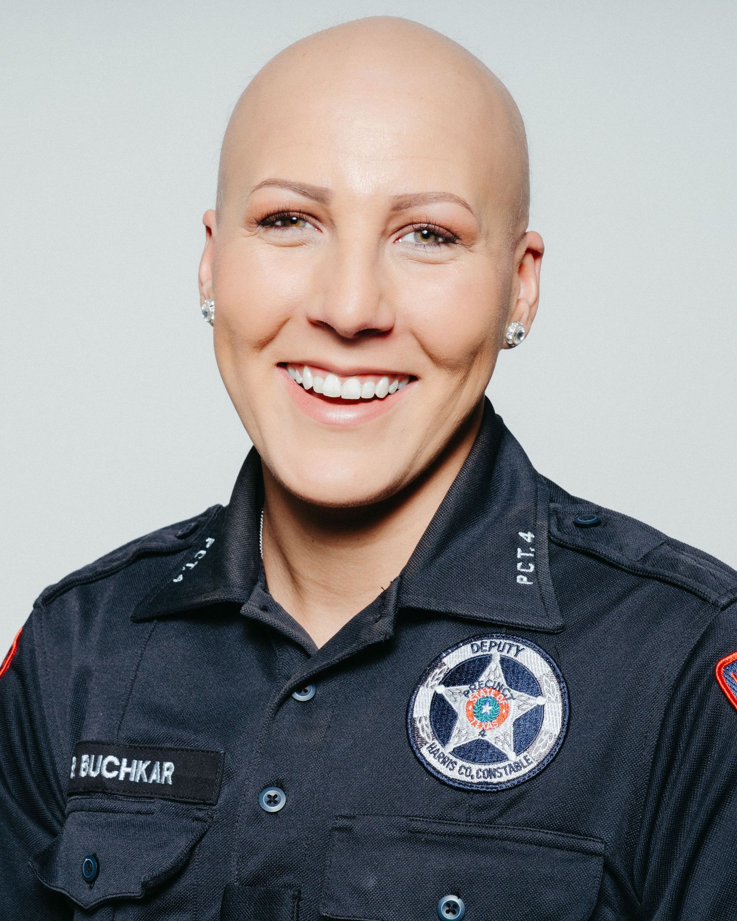 Law enforcement officer in uniform with badge and patches smiling at camera.