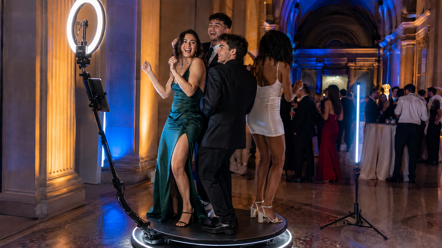 Three elegantly dressed guests pose at a photo booth during a formal gala event in a grand ballroom.