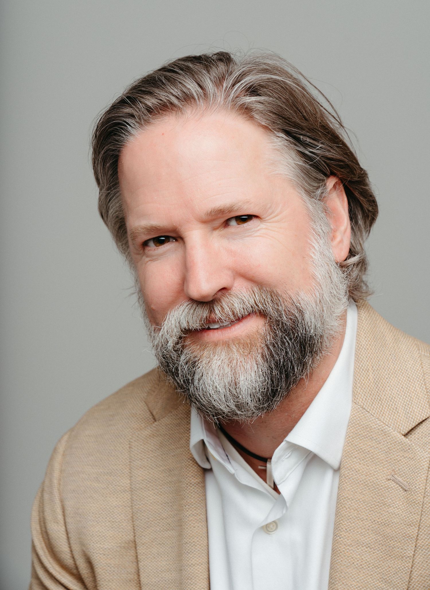 Professional portraits of a person with a beard wearing a tan blazer and white shirt.