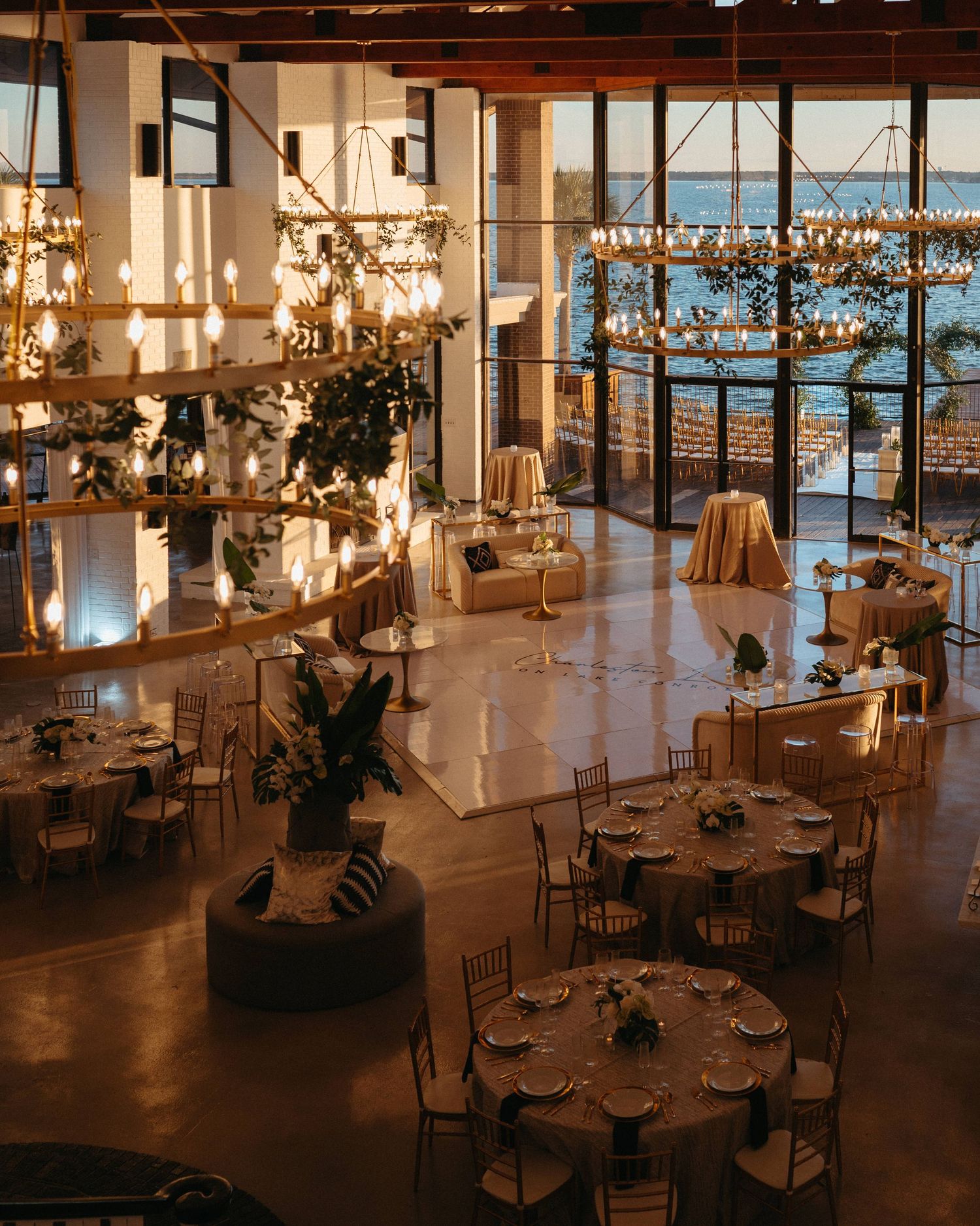 Elegant event space with round dining tables and floor-to-ceiling windows overlooking city views at sunset.