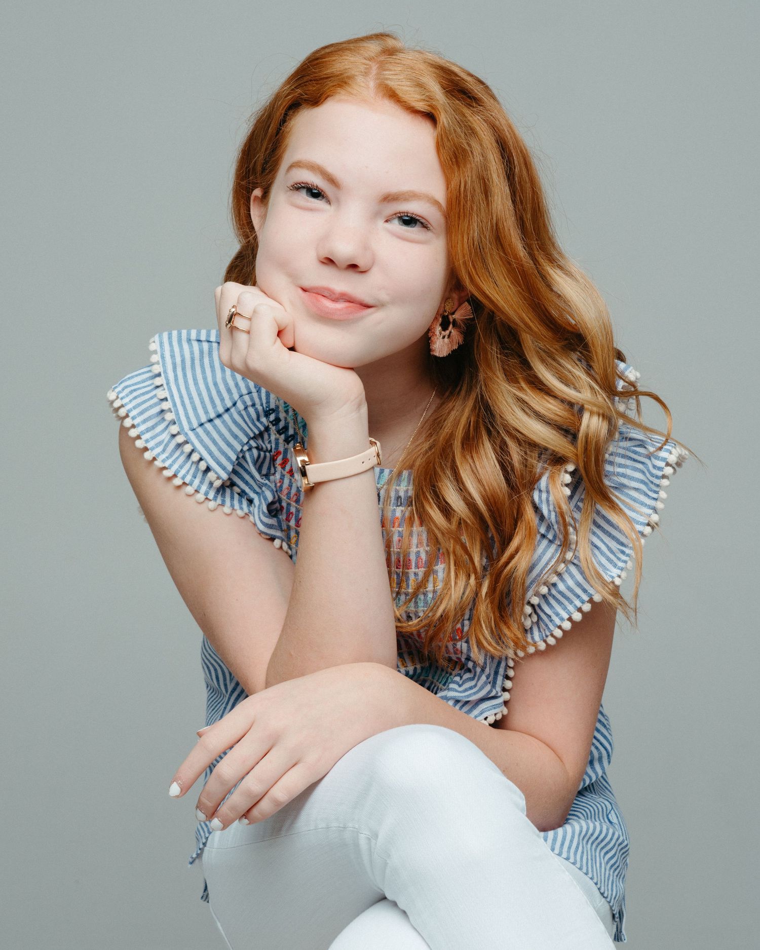 Portrait of a person with red hair wearing a ruffled blue top and posing with hand under chin.