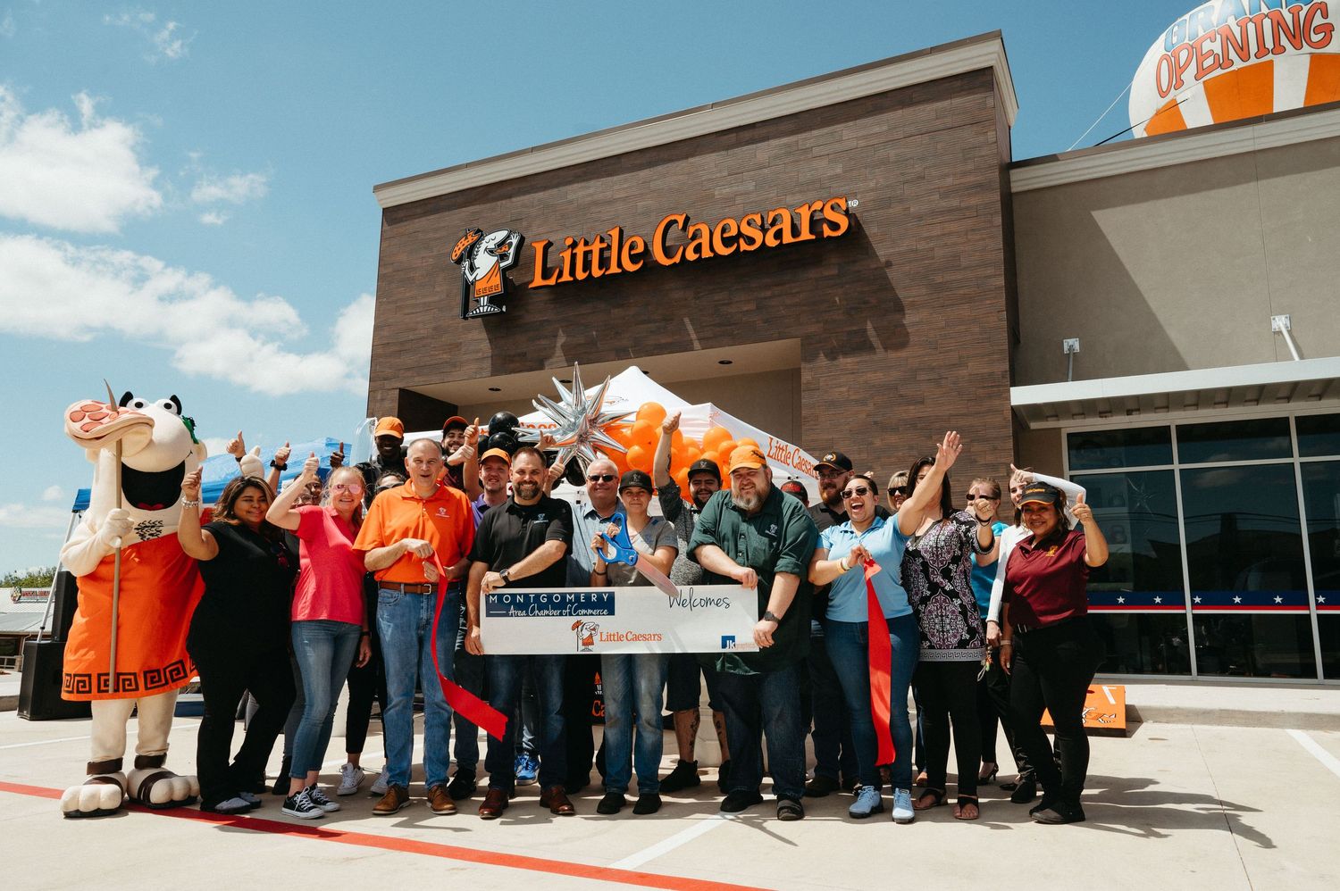 Exterior view of retail stores with customers lined up outside during grand opening event.