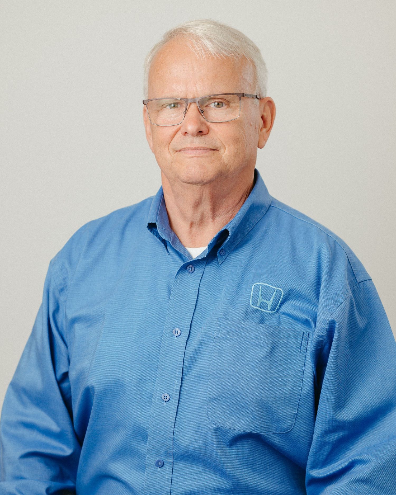 Senior professional wearing glasses and blue polo shirt in studio portraits.