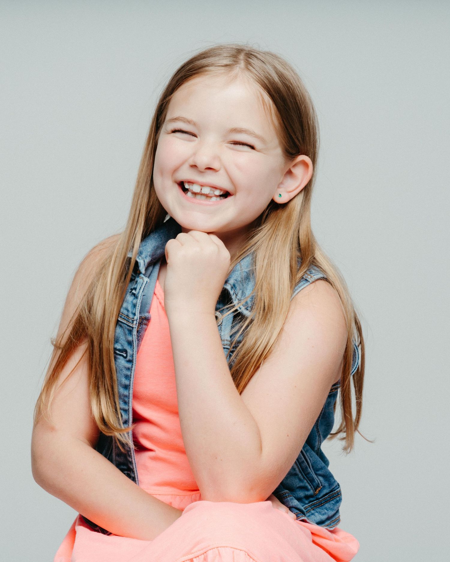 A series of candid studio portraits showing joyful expressions in a coral dress and denim vest against a light background.