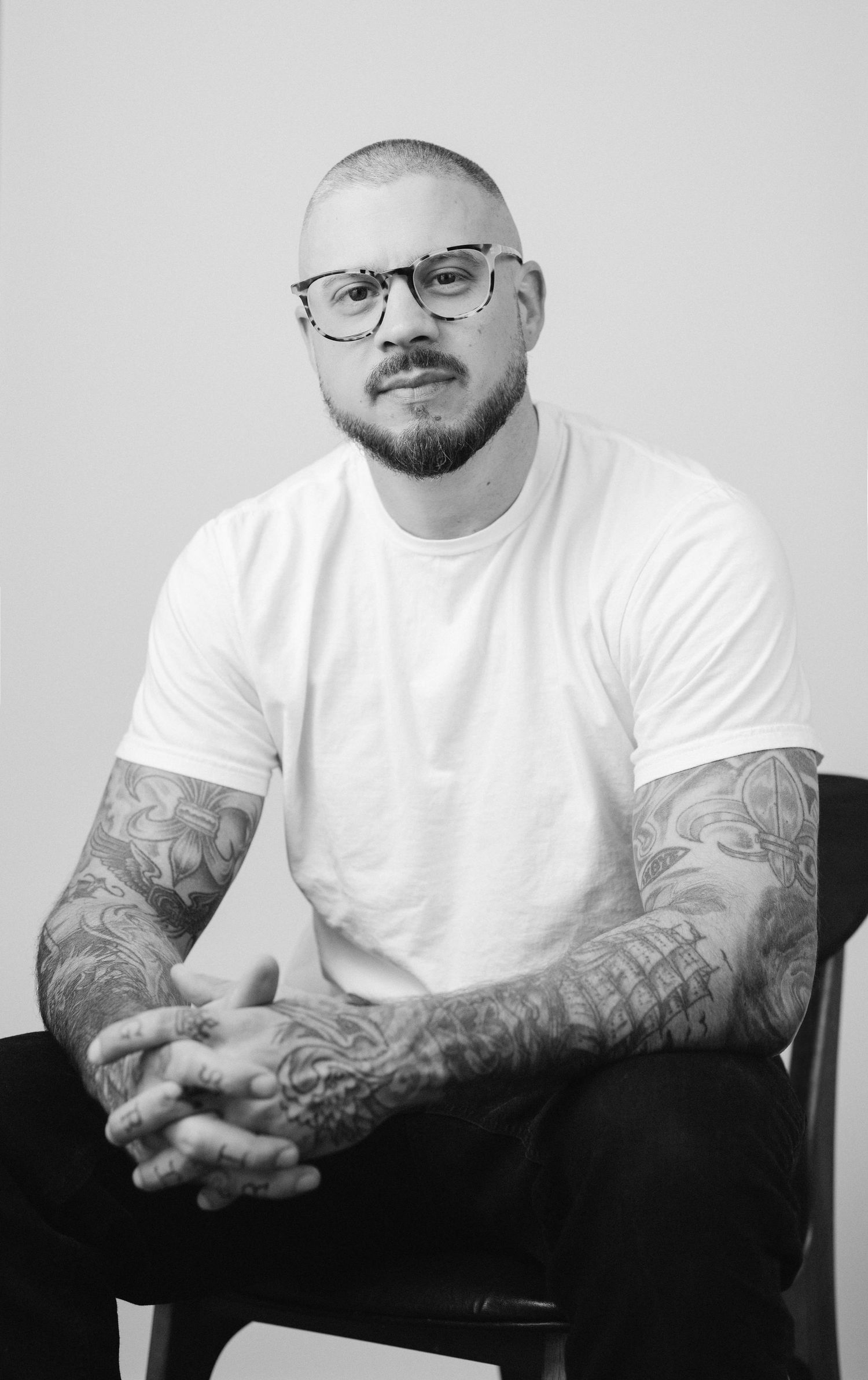 Black and white portrait series showing tattooed arms and glasses in casual white t-shirt.