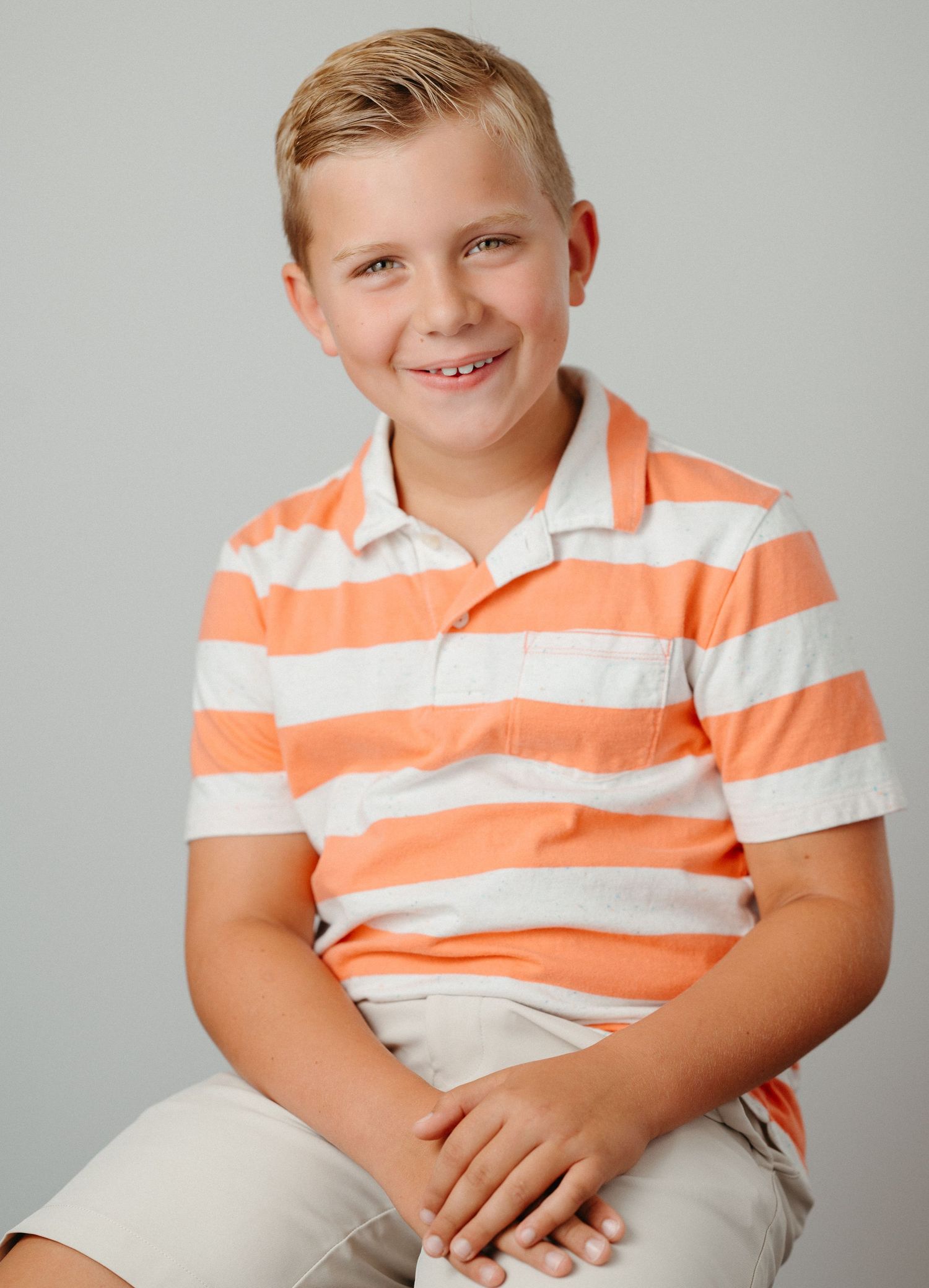 Portrait series of young person in orange striped polo shirt against light gray background.