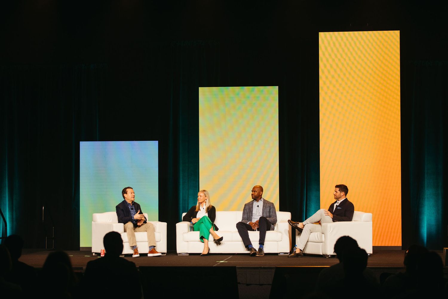 Speaker presenting on stage at a professional conference with dramatic blue and orange lighting.