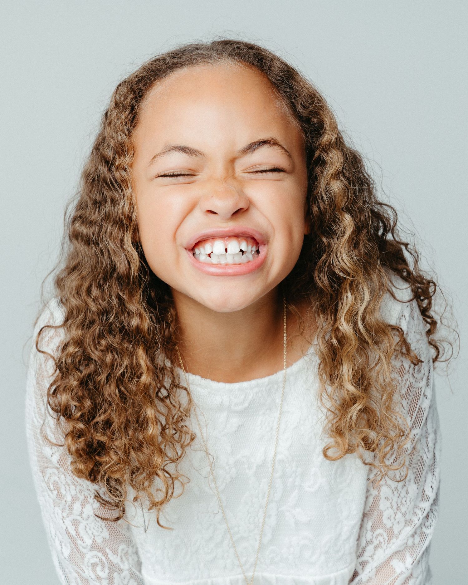 Joyful portrait of a person with curly hair wearing white lace dress and big smile.