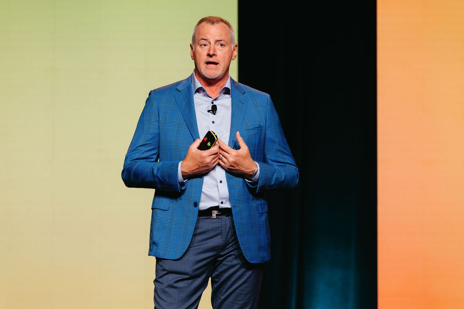 Professional speaker in a blue suit jacket gesturing during presentation on stage.