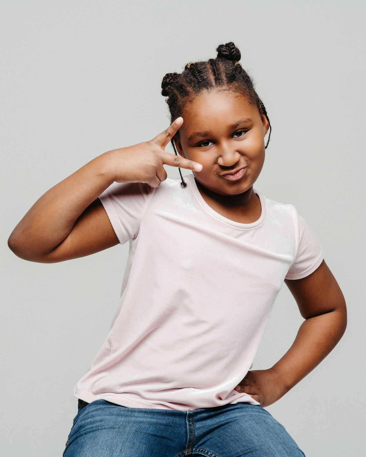 Playful portrait of a person with braided hair making peace sign gesture.