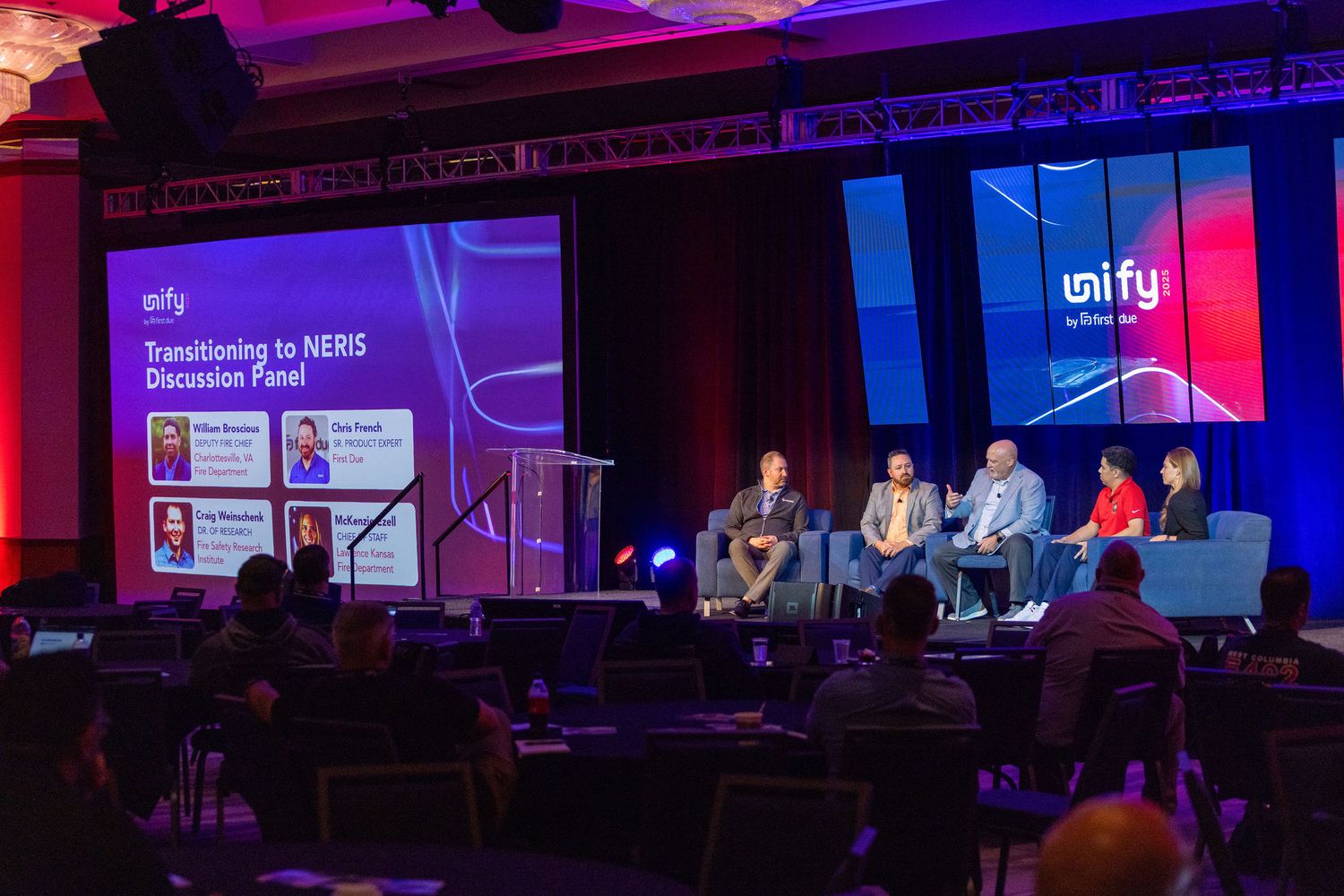 Wide view of conference stage with digital displays and dramatic red lighting effects.