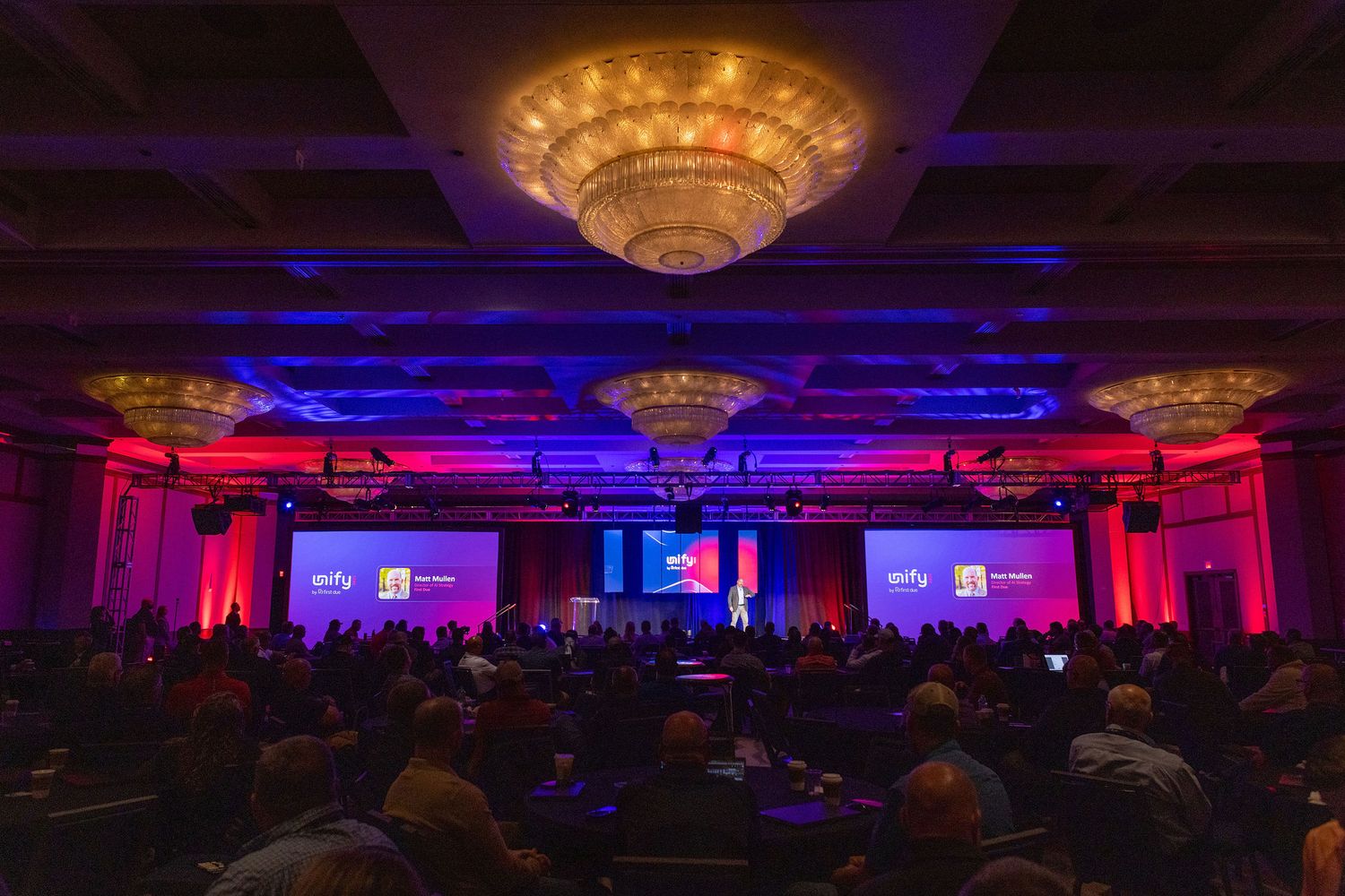 Large conference hall with elegant chandeliers and dramatic purple and blue lighting effects.