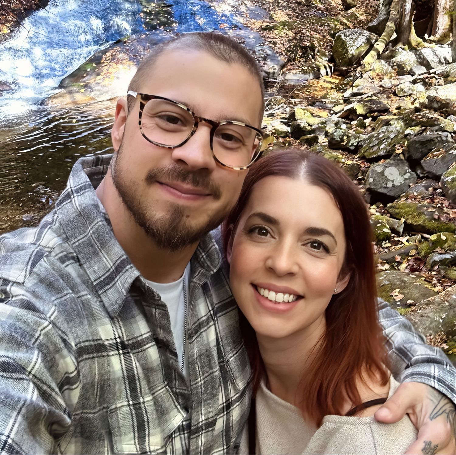 A couple takes a series of selfies together outdoors near a stream, wearing casual attire and smiling at the camera.