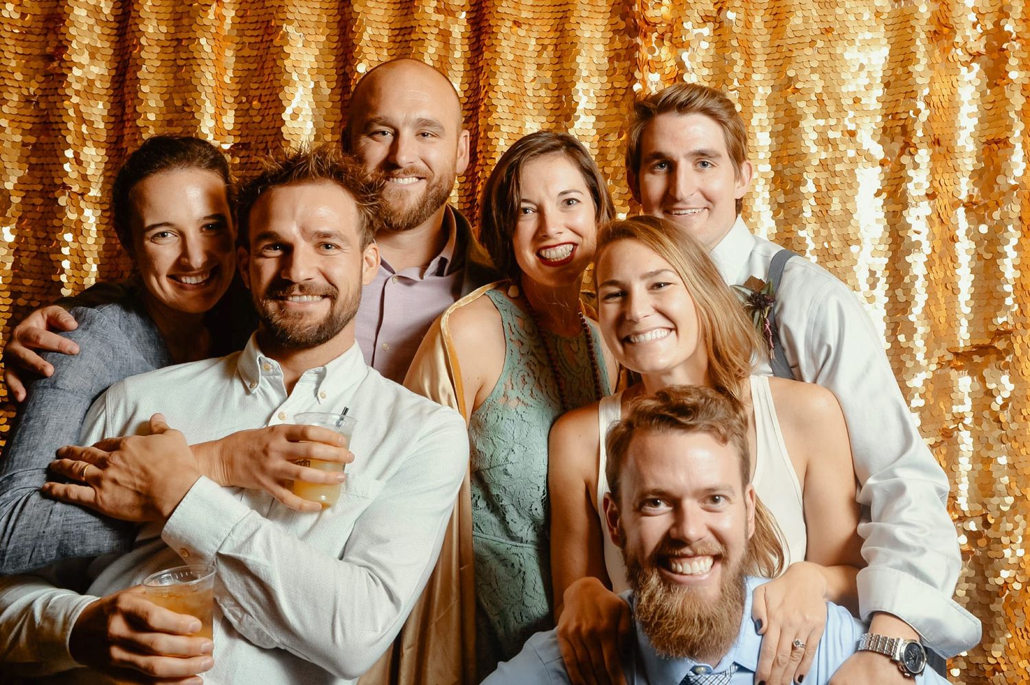 Group of friends posing and smiling in front of a gold sequin backdrop at a festive celebration.