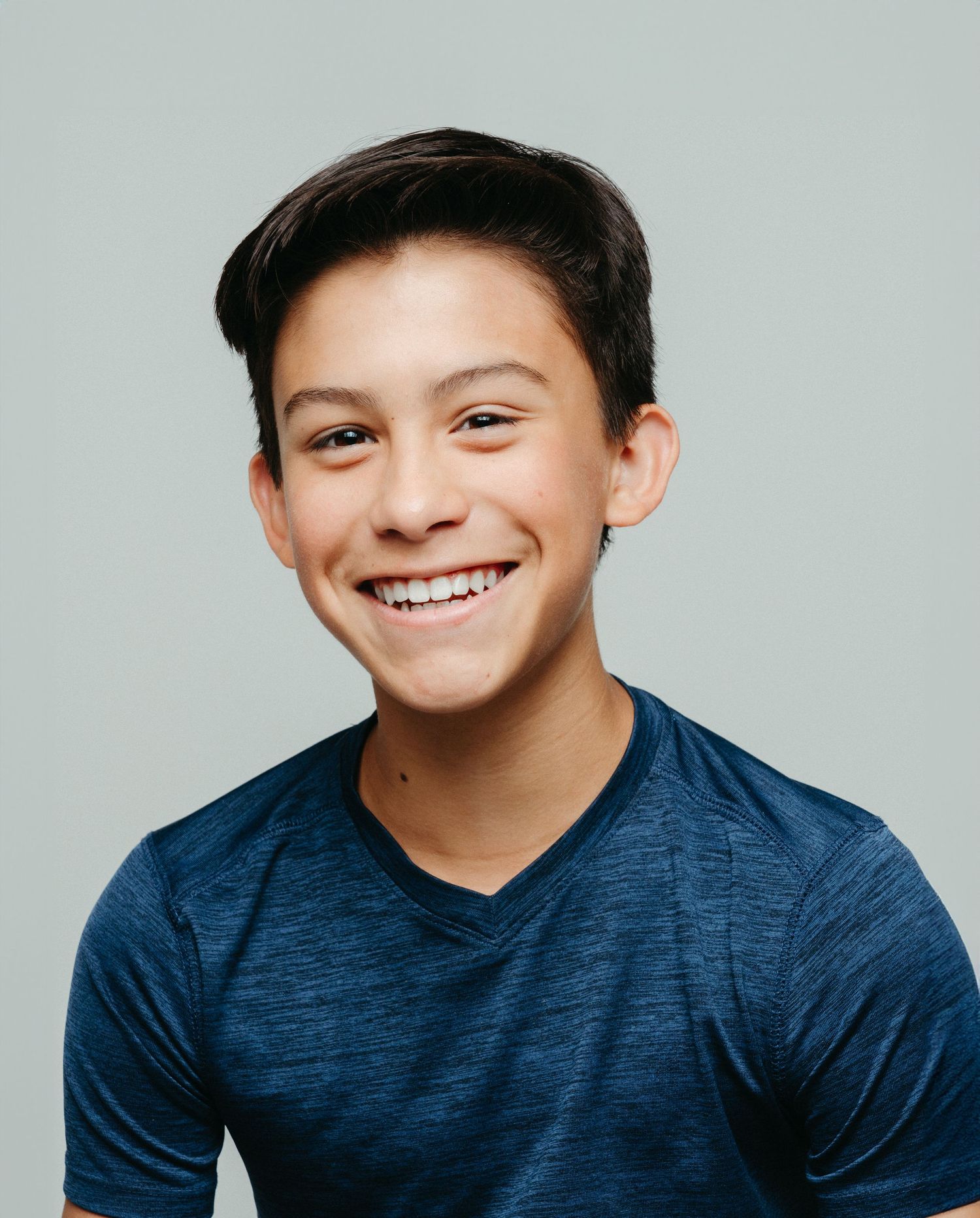 A young person in a navy blue shirt smiles warmly against a light gray background.