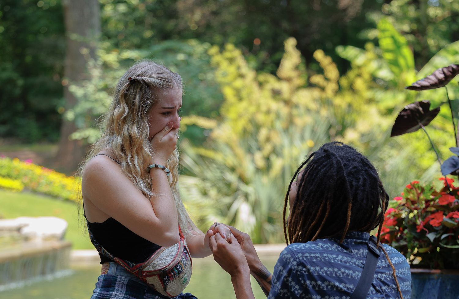 Emotional marriage proposal moment as woman covers mouth in surprise in lush garden setting.
